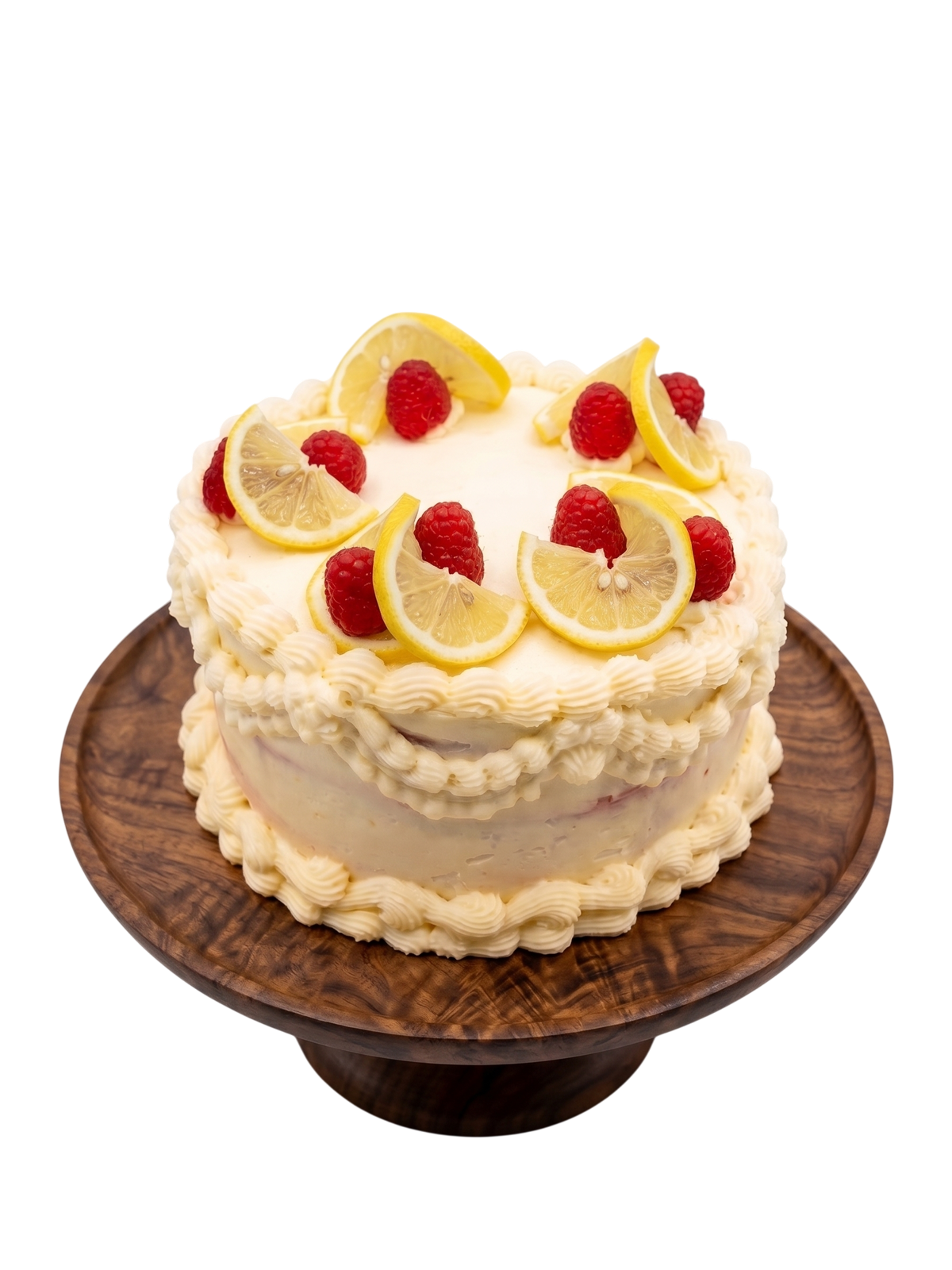 Lemon Raspberry Cake with cream frosting rosettes, fresh lemon slices, and whole raspberries on a wooden cake stand